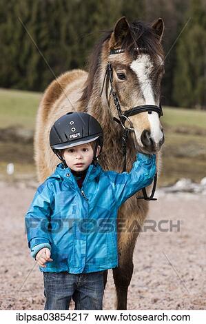 "Young child wearing a riding helmet standing beside a pony, dun, with a bridle, Tyrol, Austria, Europe" View Large Photo Image Stock Photo - "Young child wearing a riding helmet standing beside a pony, dun, with a bridle, Tyrol, Austria, Europe". Fotosearch