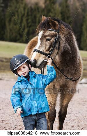 "Young child wearing a riding helmet standing beside a pony, dun, with a bridle, Tyrol, Austria, Europe" View Large Photo Image Stock Photo - "Young child wearing a riding helmet standing beside a pony, dun, with a bridle, Tyrol, Austria, Europe". Fotosearch