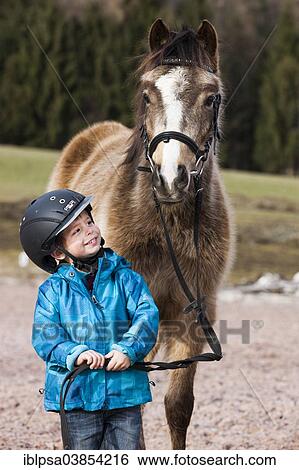 "Young child wearing a riding helmet standing beside a pony, dun, with a bridle, Tyrol, Austria, Europe" View Large Photo Image Stock Photograph - "Young child wearing a riding helmet standing beside a pony, dun, with a bridle, Tyrol, Austria, Europe". Fotosearch