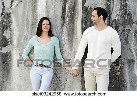"Young couple standing hand in hand in front of a wall, Austria, Europe" View Large Photo Image Stock Photo - "Young couple standing hand in hand in front of a wall, Austria, Europe". Fotosearch