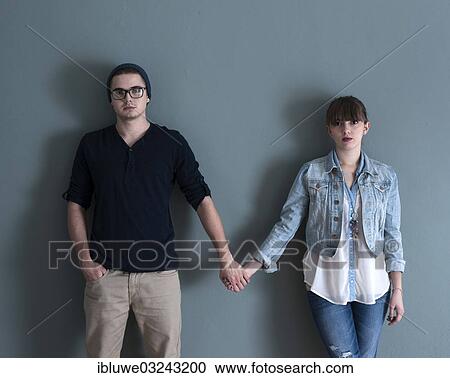 Stock Image - "Young couple standing in front of a wall, hand in hand, Mannheim, Baden-Wurttemberg, Germany, Europe". Fotosearch