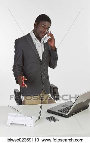 Stock Image - Young dark-skinned man holding a phone in an office. Fotosearch