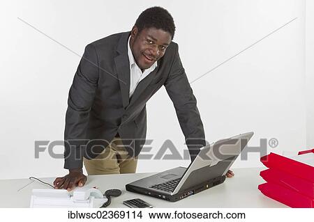 Young dark-skinned man standing at a laptop and smiling View Large Photo Image Picture - Young dark-skinned man standing at a laptop and smiling. Fotosearch
