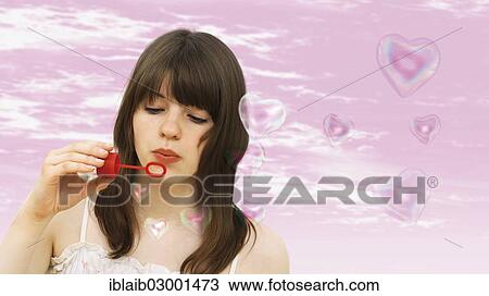 Stock Image - Young girl blowing heart-shaped soap-bubbles. Fotosearch