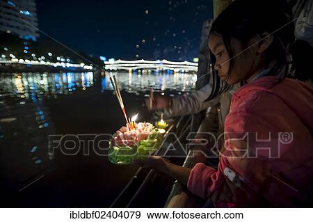 Stock Photo - "Young girl placing a ceremonial raft in the river, Loi or Loy Krathong Festival, Chiang Mai, Northern Thailand, Thailand, Asia". Fotosearch