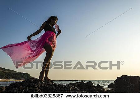 Stock Photo - "Young Indian woman wearing a pink skirt, posing on the beach, Anjuna, Goa, India, Asia". Fotosearch