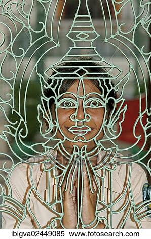 Stock Photography - "Young Khmer woman looking through a metal lattice gate with a Buddha figure, Royal Palace, Phnom Penh, Cambodia, Southeast Asia, Asia". Fotosearch