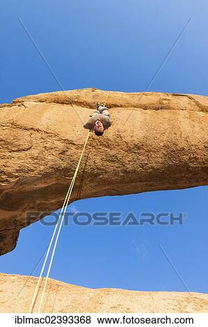 "Young man abseiling from a rock arch, hanging upside down, near the Spitzkoppe granite peaks, Damaraland, Namibia, Africa" View Large Photo Image Stock Photo - "Young man abseiling from a rock arch, hanging upside down, near the Spitzkoppe granite peaks, Damaraland, Namibia, Africa". Fotosearch
