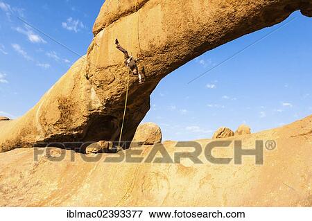 "Young man abseiling from a rock arch, hanging upside down, near the Spitzkoppe granite peaks, Damaraland, Namibia, Africa" View Large Photo Image Stock Photo - "Young man abseiling from a rock arch, hanging upside down, near the Spitzkoppe granite peaks, Damaraland, Namibia, Africa". Fotosearch