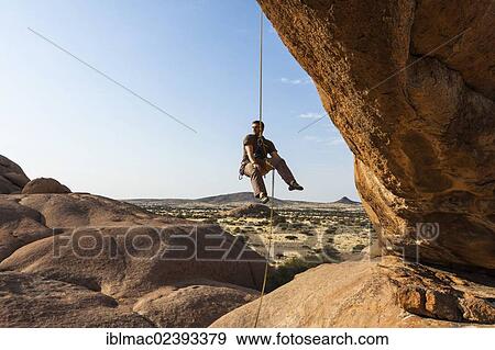 "Young man abseiling from a rock arch, near the Spitzkoppe granite peaks, Damaraland, Namibia, Africa" View Large Photo Image Stock Photo - "Young man abseiling from a rock arch, near the Spitzkoppe granite peaks, Damaraland, Namibia, Africa". Fotosearch