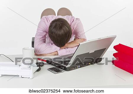 "Young man at his desk in the office with a laptop computer, head resting on the desk" View Large Photo Image Picture - "Young man at his desk in the office with a laptop computer, head resting on the desk". Fotosearch