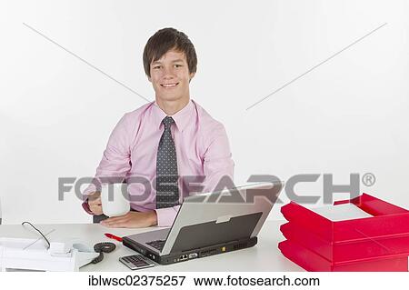 Young man at his desk in the office with a laptop computer View Large Photo Image Stock Photo - Young man at his desk in the office with a laptop computer. Fotosearch