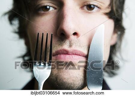 "Young man holding a knife and a fork in front of his face, Germany, Europe" View Large Photo Image Picture - "Young man holding a knife and a fork in front of his face, Germany, Europe". Fotosearch