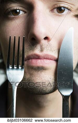 "Young man holding a knife and a fork in front of his face, Germany, Europe" View Large Photo Image Stock Image - "Young man holding a knife and a fork in front of his face, Germany, Europe". Fotosearch