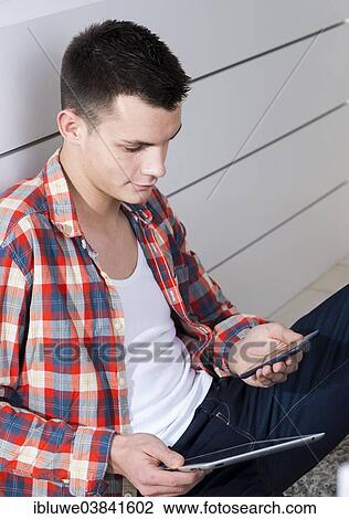 Young man holding a tablet computer and a mobile phone View Large Photo Image Stock Image - Young man holding a tablet computer and a mobile phone. Fotosearch