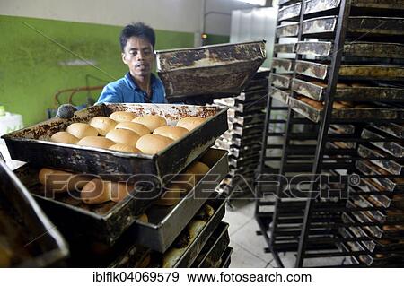 Stock Photo - "Young man in a bakery taking bread out of the oven, Gampong Nusa, Aceh province, Indonesia, Asia". Fotosearch