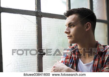 Young man looking out of a window View Large Photo Image Stock Image - Young man looking out of a window. Fotosearch