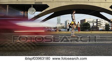 Stock Image - "Young man painted in Polynesian patterns standing on a street as a car drives by, Berlin, Germany, Europe". Fotosearch