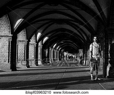 Stock Image - "Young man painted in Polynesian patterns standing under arches, Oberbaumbrucke bridge, Berlin, Germany, Europe". Fotosearch