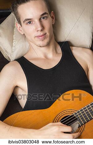 Young man relaxing and playing his acoustic guitar View Large Photo Image Stock Photo - Young man relaxing and playing his acoustic guitar. Fotosearch
