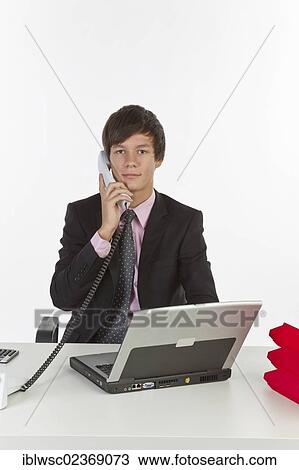 Young man sitting at a laptop and holding a phone View Large Photo Image Stock Image - Young man sitting at a laptop and holding a phone. Fotosearch