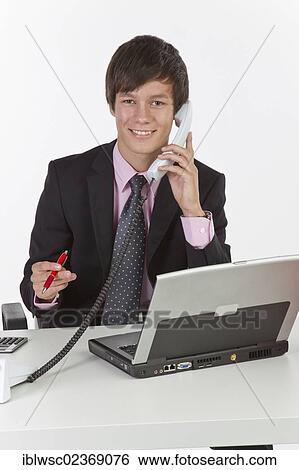 Young man sitting at a laptop and holding a phone View Large Photo Image Stock Photograph - Young man sitting at a laptop and holding a phone. Fotosearch