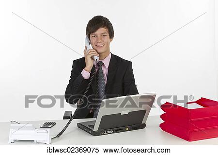 Young man sitting at a laptop and holding a phone View Large Photo Image Stock Photography - Young man sitting at a laptop and holding a phone. Fotosearch