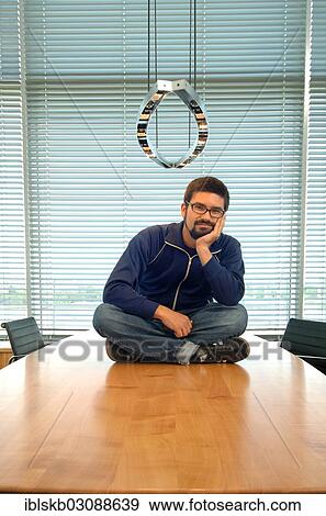 Young man sitting cross-legged on a conference desk View Large Photo Image Stock Photo - Young man sitting cross-legged on a conference desk. Fotosearch