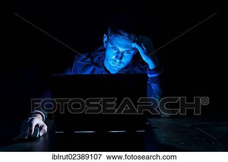 "Young man sitting in front of a laptop in the dark, illuminated only by the monitor" View Large Photo Image Stock Photo - "Young man sitting in front of a laptop in the dark, illuminated only by the monitor". Fotosearch
