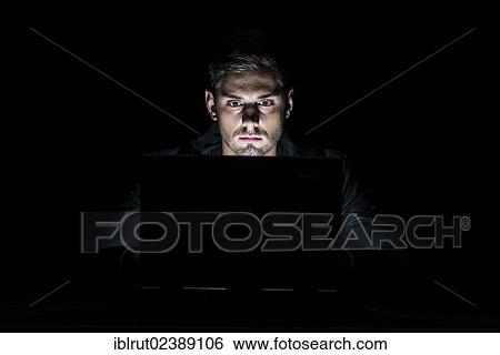 "Young man sitting in front of a laptop in the dark, illuminated only by the monitor" View Large Photo Image Stock Photograph - "Young man sitting in front of a laptop in the dark, illuminated only by the monitor". Fotosearch