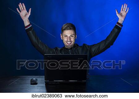 "Young man sitting in the dark in front of a laptop, with a joyful expression, exulting" View Large Photo Image Stock Image - "Young man sitting in the dark in front of a laptop, with a joyful expression, exulting". Fotosearch