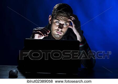 "Young man sitting in the dark in front of a laptop, with a thoughtful expression" View Large Photo Image Stock Photo - "Young man sitting in the dark in front of a laptop, with a thoughtful expression". Fotosearch