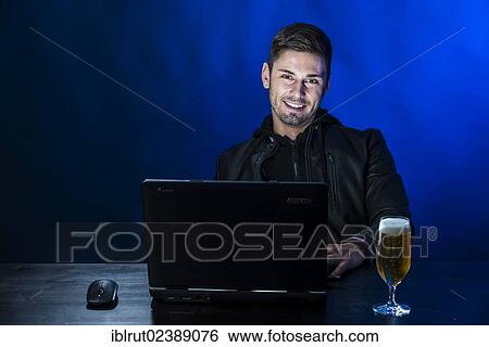 "Young man sitting in the dark in front of his laptop, with a beer beside him, symbolic image about computer addiction and alcoholism" View Large Photo Image Stock Photograph - "Young man sitting in the dark in front of his laptop, with a beer beside him, symbolic image about computer addiction and alcoholism". Fotosearch
