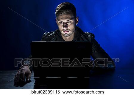 Stock Photography - Young man sitting in the dark in front of a laptop. Fotosearch