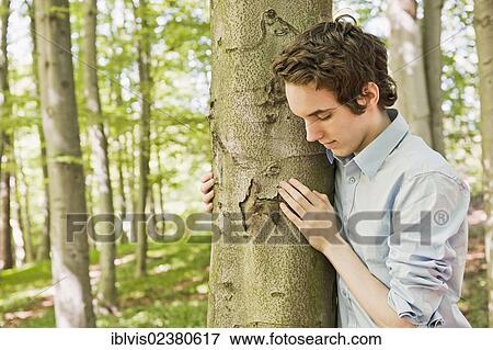 Young man standing by a tree in the woods View Large Photo Image Stock Photo - Young man standing by a tree in the woods. Fotosearch