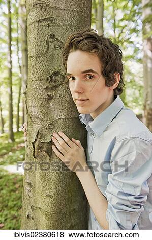 Stock Photo - Young man standing by a tree in the woods. Fotosearch