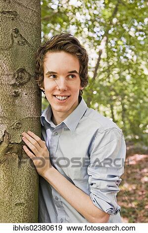 Young man standing by a tree in the woods View Large Photo Image Stock Photo - Young man standing by a tree in the woods. Fotosearch