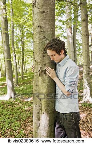 Young man standing by a tree in the woods View Large Photo Image Stock Photograph - Young man standing by a tree in the woods. Fotosearch