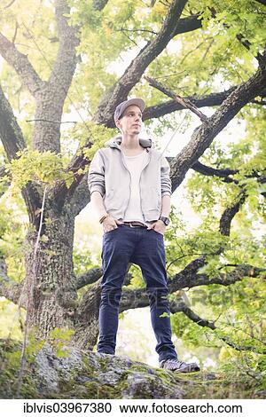 Young man standing by himself in a forest View Large Photo Image Stock Image - Young man standing by himself in a forest. Fotosearch