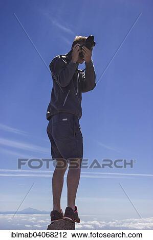 "Young man taking a photo whilst standing on a rock, island of Tenerife with Mount Teide at the back, """"Ruta de los Volcanes"""", Volcano Route, Cumbre Vieja Natural Park, La Palma, Canary Islands, Spain, Europe" View Large Photo Image Stock Image - "Young man taking a photo whilst standing on a rock, island of Tenerife with Mount Teide at the back, """"Ruta de los Volcanes"""", Volcano Route, Cumbre Vieja Natural Park, La Palma, Canary Islands, Spain, Europe". Fotosearch
