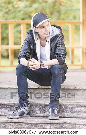 Stock Photo - "Young man wearing a leather jacket, sitting in a park". Fotosearch