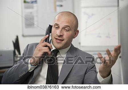 Stock Image - Young man wearing a suit is talking on a phone in the office. Fotosearch
