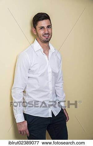Young man wearing a white shirt leaning against a wall View Large Photo Image Stock Photo - Young man wearing a white shirt leaning against a wall. Fotosearch