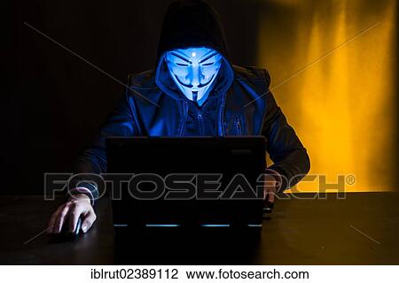 Young man wearing an anonymous mask and a hood sitting in front of a laptop View Large Photo Image Stock Image - Young man wearing an anonymous mask and a hood sitting in front of a laptop. Fotosearch