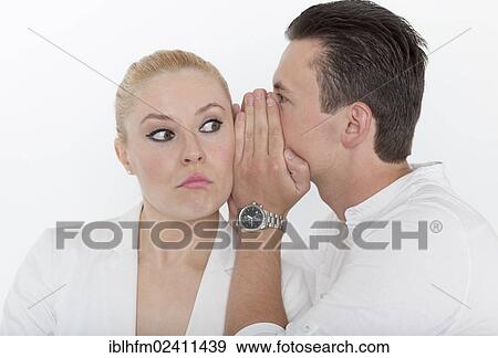 Stock Photo - "Young man whispering something into the ear of his young partner, which she receives with a skeptical look, symbolic image for unpleasant news". Fotosearch
