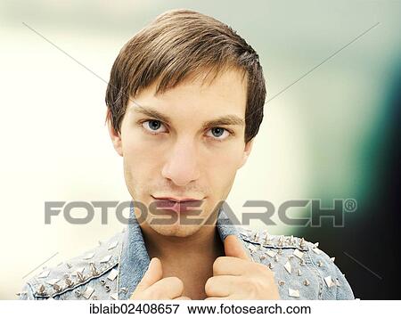 Stock Photo - "Young man with a serious face wearing a studded denim jacket, portrait". Fotosearch