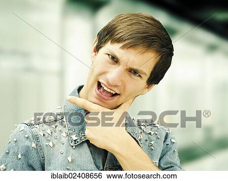 Stock Photograph - "Young man with a serious face wearing a studded denim jacket, cheeky gesture, portrait". Fotosearch