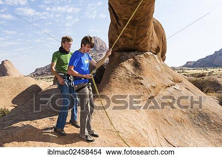 Picture - "Young men hanging in a climbing rope, Bogenfels, Spitzkoppe, Namibia, Africa". Fotosearch