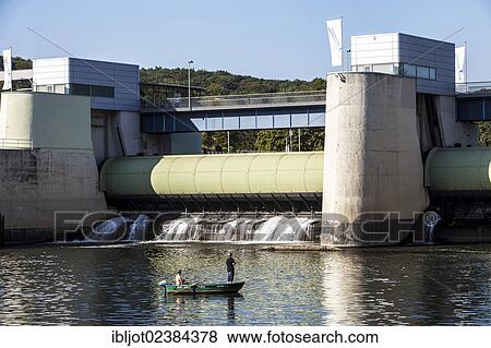 Stock Photo - "Young men in a rowing boat with an outboard engine fishing on the Ruhr river, in front of the dam of lake Baldeneysee, Essen, North Rhine-Westphalia, Germany, Europe". Fotosearch