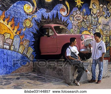 "Young men talking in front of a sculpture of a car breaking through a wall, entrance to a youth club, Chiang Rai, Chiang Rai Province, Northern Thailand, Thailand, Asia" View Large Photo Image Stock Photo - "Young men talking in front of a sculpture of a car breaking through a wall, entrance to a youth club, Chiang Rai, Chiang Rai Province, Northern Thailand, Thailand, Asia". Fotosearch